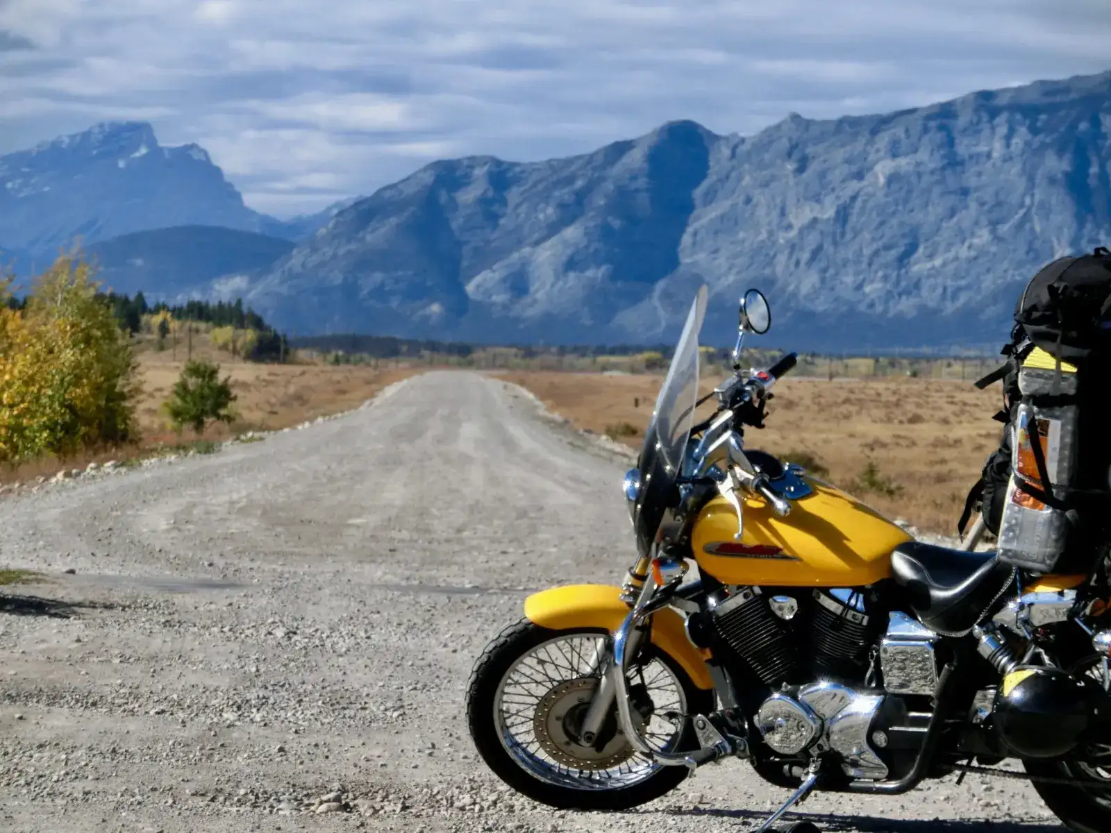 A loaded motorcycle on a wide gravel road with forest and mountains ahead