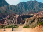 A motorcycle rider on a paved road approaching the red rock formations of the Quebrada de las Conchas near Cafayate, Argentina.