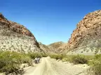 Motorcycle on a gravel road through a rocky Patagonian canyon under clear blue sky.