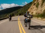 Two adventure motorcycles riding on a paved road through forested Patagonian mountains in Argentina.