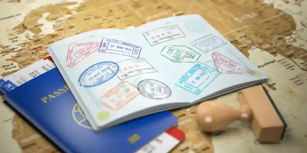 An open passport with visa stamps on a world map, next to a second passport, boarding passes, and a rubber stamp.