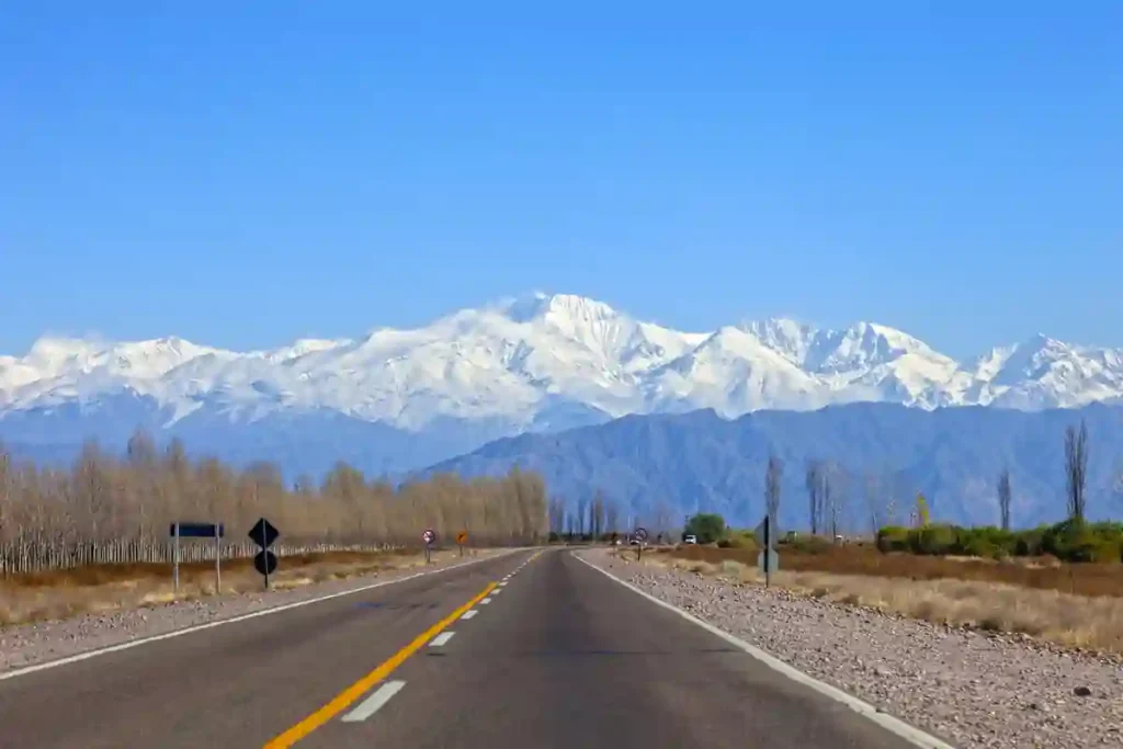 An empty paved highway heads toward the snow-covered Andes near Mendoza, Argentina.